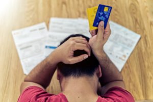 Hombre agobiado revisando facturas y deudas con tarjetas de crédito
