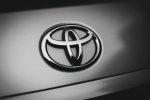 Llave de coche Toyota sobre una mesa junto a monedas apiladas y manos usando una calculadora, representando el cartel de los coches Toyota y su gestión económica.