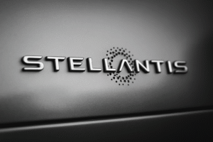 Filas ascendentes de monedas apiladas frente a un coche en miniatura y el logotipo de Stellantis, simbolizando el cartel de los coches Stellantis y su estrategia económica.